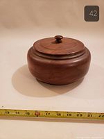 Side view of round wooden container with lid, measuring tape shows diameter