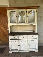 Front view of entire distressed white kitchen hutch showing upper glass doors and lower drawers and cabinets