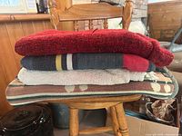 Stack of four folded throw blankets on chair showing colors and textures