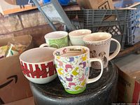 Five mugs and one patterned bowl on black surface
