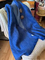 Ruana draped on chair showing cobalt blue exterior, grey interior, two wooden buttons, fringe hem