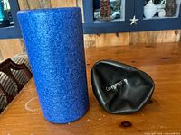 Blue foam roller standing next to deflated black Coregeous ball on wooden table