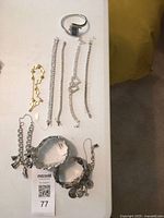 Overall view of watch, slender rhinestone bracelets, gold-tone bracelet, wide cuffs and charm bracelets on table