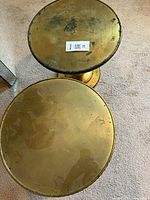 Top view of both round gold pedestal tables showing glass surface and finish wear