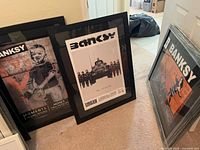 Three framed Banksy prints leaning against wall