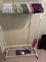 Front view of white rolling rack with assorted velvet hangers and sealed purple packs