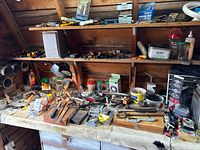 Overall view of crowded workbench showing variety of hand tools, measuring tools and hardware