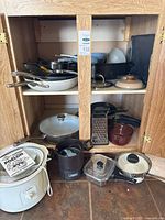 Cabinet showing multiple stainless and non-stick pans, box grater, storage container and lids