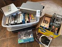 All items grouped: DVD player, VCR, CD player box, cleaner, headphones, bins of tapes and DVDs