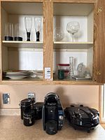 Cabinet and countertop view showing plates, glassware, storage containers, vase, tumbler, coffee maker, canisters, griddle