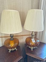 Pair of matching amber glass table lamps with shades on wooden tables