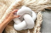 Hand holding white plush knot pillow on faux fur surface