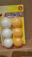 Front view of one blister pack showing three white and three orange balls