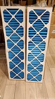 Two identical blue pleated HVAC filters standing side by side