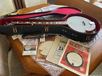 Banjo in open hard case with books, strings, strap displayed