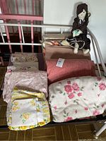 Stack of blankets, sheets, two mats and rag doll on bed frame