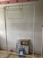 Two silver metal clothing racks, one assembled, garment bags in packaging at base