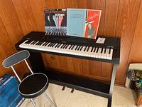 Front view of Casio COS 700 digital piano on stand with stool, books displayed on music rack area