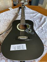 Full view of black acoustic guitar and attached strap on table