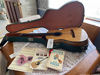 Guitar in open green hard case with three instructional books laid out beside it