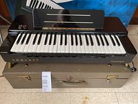 Front view of Hohner Organet on its case showing keys, music stand, control knobs and branding