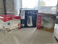 Three boxed kettles on table: Melitta whistling kettle, HB PRO cordless electric kettle, Rival Hot Pot Express