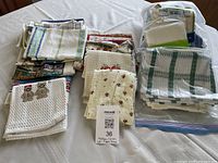 Grouped view of folded tea towels with various patterns and bagged knitted dishcloths