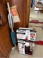 Shark vacuum box beside Hoover broom and vacuum bag package