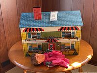Front exterior of tin dollhouse with puppet laid in front