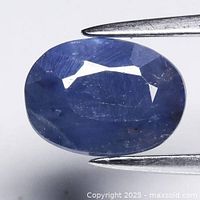 Close-up of the oval blue sapphire held in gem tweezers