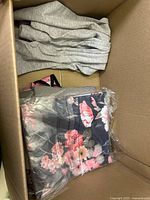 Open box showing grey knitwear and packaged navy floral print garment