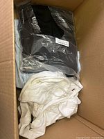 Top view of box showing black garment in plastic, light blue item and white knit top