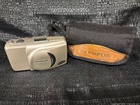 Front view of Olympus Stylus Zoom 115 camera next to branded soft case