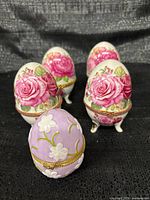 Front view of all five egg trinket boxes displaying floral designs and tripod feet