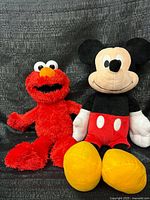 Tickle Me Elmo and Mickey Mouse plush side by side