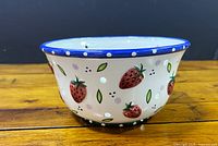 side view of porcelain colander showing strawberry pattern and blue rim