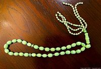 Full view of light green gemstone rosary laid flat showing bead arrangement and tassel