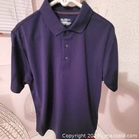 Front view of navy Ben Hogan polo on hanger