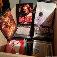 Open box showing assortment of DVDs and CDs, visible AC/DC, Rush, Jimi Hendrix covers