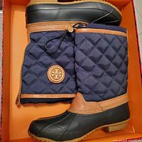 Boots in box, side profile showing quilted shaft, leather trim, Tory Burch logo medallion