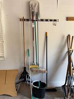 All cleaning tools bundled against wall including mops, dustpans, buckets