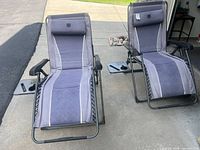 Two Timber Ridge zero-gravity folding lounge chairs with headrests and side trays positioned on driveway
