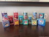 All seven Burger King Disney cups and Little Mermaid mug with packaging displayed on tabletop