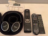 All five items laid out: headphones in case, Sunlabz charger, Logitech remote, generic remote, Sharp remote