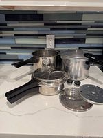Both pressure cooker bodies, universal lid, trays and weights displayed together