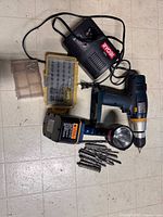 All items laid out: drill, flashlight, charger, battery, bit case, loose bits