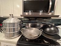 Group shot of two-tier steamer and three woks on stovetop