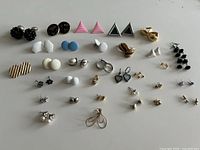 All 34 pairs of assorted stud earrings laid out on white surface
