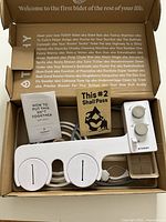 Open box showing TUSHY bidet attachment, hose, hardware, booklet and card