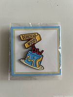 Front view of sealed Donovan Woods enamel pin on backing card